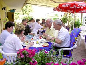 Several adults sitting at outdoor patio tables under umbrellas enjoying a meal at G&auml;stehaus Rita