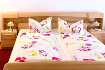Twin beds with floral patterned bedding and matching pillows in a wooden frame at G&auml;stehaus Rita room with bedside lamps