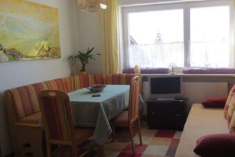 Dining area with striped cushioned bench, wooden chairs, table with tablecloth and TV in Pension G&auml;stehaus Alpenblick