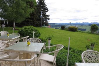 Outdoor seating area with white wicker chairs and glass tables overlooking a green lawn and distant mountains at Pension G&auml;stehaus Alpenblick