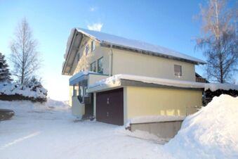 A yellow two-story building with snow on the roof and ground near trees under a clear sky at Pension G&auml;stehaus Alpenblick