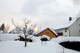 Snow-covered garden with leafless trees and houses in the background at Pension G&auml;stehaus Alpenblick during wintertime