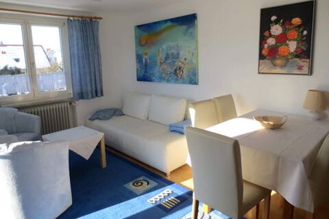 Living room in Pension G&auml;stehaus Alpenblick with white sofa, dining table, blue carpet, and wall paintings near window