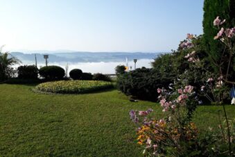 Garden with green lawn, trimmed bushes, and flowers at Pension G&auml;stehaus Alpenblick with hills and fog in background
