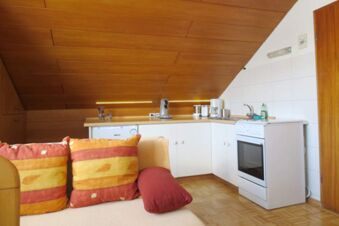 Small attic kitchen with white cabinets, stove, coffee maker, and colorful pillows on sofa at Pension G&auml;stehaus Alpenblick