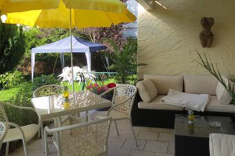 Outdoor patio area at Pension G&auml;stehaus Alpenblick featuring white chairs, yellow umbrella, and beige cushioned sofa surrounded by plants