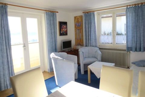Living room with blue curtains, two light blue armchairs, a small television, and a table at Pension G&auml;stehaus Alpenblick