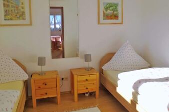 Two single wooden beds with floral bedding, two wooden nightstands with lamps, and a mirror in Pension G&auml;stehaus Alpenblick