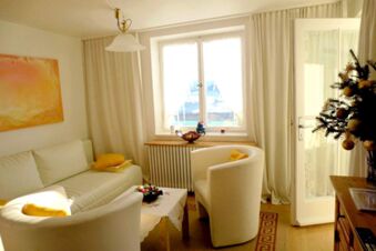 Sunlit living room with white sofa, two armchairs, a window, and a Christmas tree at Pension G&auml;stehaus Alpenblick