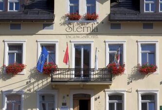 Facade of Akzent Hotel Goldner Stern featuring multiple windows with flower boxes, a balcony with three flags, and the hotel name on the wall