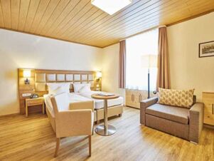 Hotel room at Akzent Hotel Goldner Stern with a double bed, beige armchair, small round table, and a gray sofa by the window