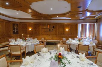 Dining room with wooden paneling and round tables set with white linens and candles at Akzent Hotel Goldner Stern