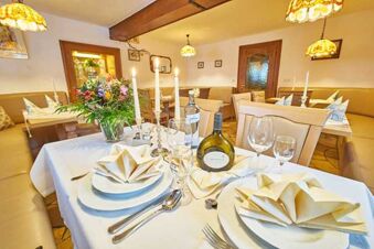 A dining table set with folded napkins, candles, glasses, and a bottle in the restaurant of Akzent Hotel Goldner Stern