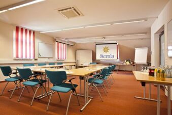Conference room with blue chairs, wooden tables, red striped window blinds, and a projection screen at Akzent Hotel Goldner Stern