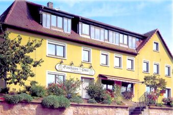 Die gelbe Fassade des Gasthauses Zur Post mit vielen Fenstern, Blumenbepflanzung und einem schr&auml;gen Dach an einem sonnigen Tag.