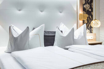 Modern und elegant eingerichtetes Hotelzimmer mit wei&szlig;en Kissen und Bettw&auml;sche im Gasthof-Metzgerei St&ouml;berl mit stilvoller Beleuchtung.