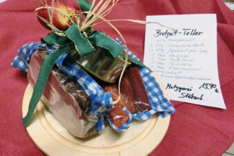 Geschenkpaket mit verschiedenen Wurstwaren und Aufschnitt, dekoriert mit gr&uuml;nem Band, auf Holzbrett pr&auml;sentiert, Gasthof-Metzgerei St&ouml;berl