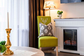 Gem&uuml;tlicher Sitzbereich mit gr&uuml;nem Stuhl, dekorativem Kissen und Kamin im stilvollen Ambiente des Gasthof-Metzgerei St&ouml;berl.