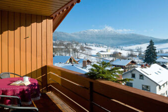 Balkon des Gasthof-Metzgerei St&ouml;berl mit Tisch, Buch und Tasse, Blick auf schneebedeckte H&auml;user und Berge bei klarem Himmel.