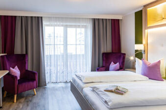 Modern eingerichtetes Doppelzimmer mit zwei Betten, lila Sesseln und gro&szlig;en Fenstern im Gasthof-Metzgerei St&ouml;berl.