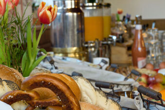 Frisches Geb&auml;ck wie Brezeln und Br&ouml;tchen sowie Orangensaft und Blumen Teil eines Fr&uuml;hst&uuml;cksbuffets im Gasthof-Metzgerei St&ouml;berl