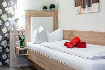 Modern eingerichtetes Einzelzimmer mit Holzbettrahmen, wei&szlig;en Bettw&auml;sche und roten Handt&uuml;chern im Gasthof-Metzgerei St&ouml;berl.