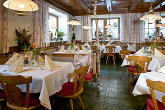 Gasthof-Metzgerei St&ouml;berl zeigt ein rustikales Restaurant mit wei&szlig;en Tischdecken, Holzm&ouml;beln und dekorativen Blumen auf den Tischen.