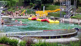 People swimming and playing on inflatable structures in a pool with slides and diving platforms at Hotel Post Nordhalben