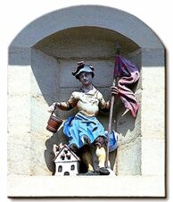 Statue of a seated figure holding a bucket and a purple flag, placed in a stone niche at Hotel Post Nordhalben