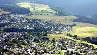 Aerial view of a village with houses and fields surrounded by hills and forests near Hotel Post Nordhalben