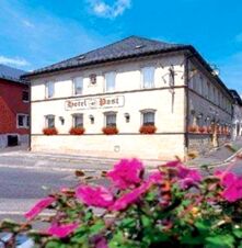 Hotel Post Nordhalben building with white walls and flower boxes under windows on a sunny day with pink flowers in foreground