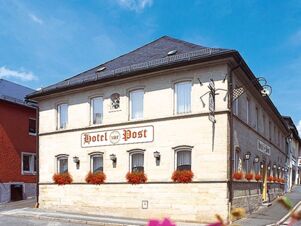 Hotel Post Nordhalben building with beige walls, flower boxes under windows, and a streetlamp on a sunny day