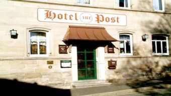Front entrance of Hotel Post Nordhalben with a green door, brown canopy, and stone facade with windows and signage