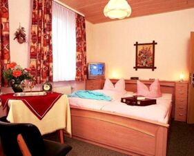 A cozy hotel room at Hotel Post Nordhalben with a double bed, bedside tables, a small TV, and a window with patterned curtains