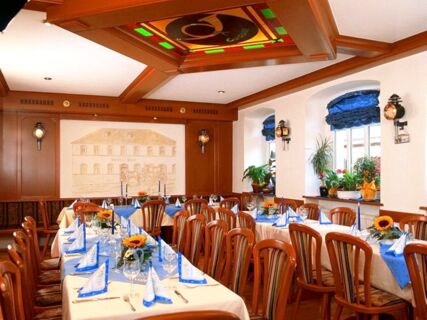 Dining area at Hotel Post Nordhalben with wooden chairs, tables set with blue napkins, glassware, and sunflowers on windowsills