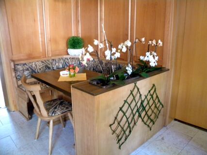 Wood-paneled corner seating area with a wooden table and chairs, orchids, and a small flower arrangement at Hotel M&auml;rkischer Landmann