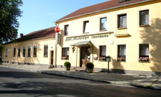 Yellow fa&ccedil;ade of Hotel M&auml;rkischer Landmann with several windows, flower boxes, potted plants, and a Coca-Cola hotel sign