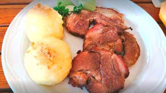 Ein Teller mit zwei Kartoffelkn&ouml;deln und mehreren Scheiben Bratenfleisch, serviert im Gasthof Waldbrunner Hof mit frischer Petersilie als Garnitur.
