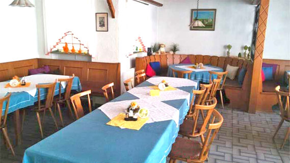 Gem&uuml;tlicher Gastraum mit blauen Tischdecken, Holzm&ouml;beln und dekorativen Details im Gasthof Waldbrunner Hof f&uuml;r entspannte Mahlzeiten.
