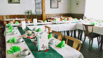 Das Restaurant des Gasthof Waldbrunner Hof ist festlich mit gr&uuml;nen Servietten, wei&szlig;en Tischen und Geschirr f&uuml;r ein Event dekoriert.