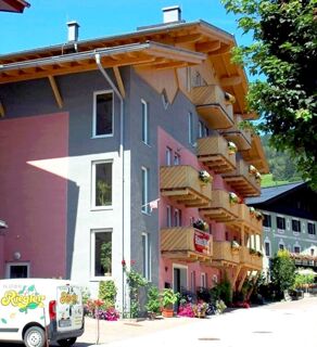 A multi-story building with wooden balconies decorated with flowers and a "Pension Haus Pilch" sign on the facade