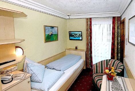Single bed with light blue bedding in a room at Pension Haus Pilch with a small table, striped chair, and wall-mounted TV