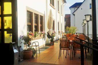 Outdoor seating area with wooden chairs and tables along a building wall with flower boxes at Posthotel Johannesberg