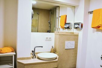 Ba&ntilde;o limpio y moderno con lavabo, espejo y toallas naranjas en el Posthotel Johannesberg.