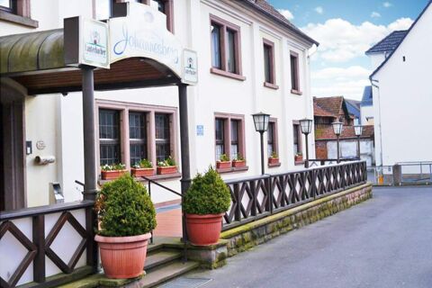 Entrance of Posthotel Johannesberg with white walls, several windows with flower boxes, two potted plants, and street lamps along a wooden fence