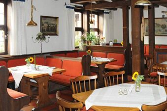 Dining area with wooden tables, orange cushioned benches, sunflowers in glass vases, and white curtains at Posthotel Johannesberg