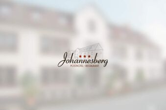 El logotipo del Posthotel Johannesberg puede verse delante de un edificio borroso que presumiblemente representa el hotel, un t&iacute;pico edificio hotelero con varias ventanas.