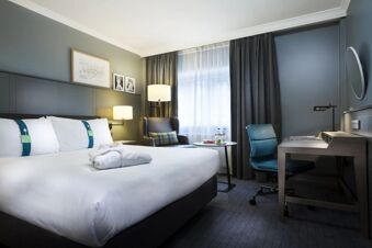 Hotel room at Holiday Inn London-Regent's Park featuring a large bed with white linens, an armchair, desk, and window with curtains
