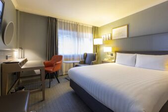 Hotel room at Holiday Inn London-Regent's Park with a large bed, two chairs, a desk, and soft lighting next to a window