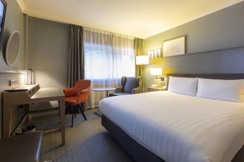 Hotel room at Holiday Inn London-Regent's Park with a large bed, two chairs, a desk, and soft lighting next to a window